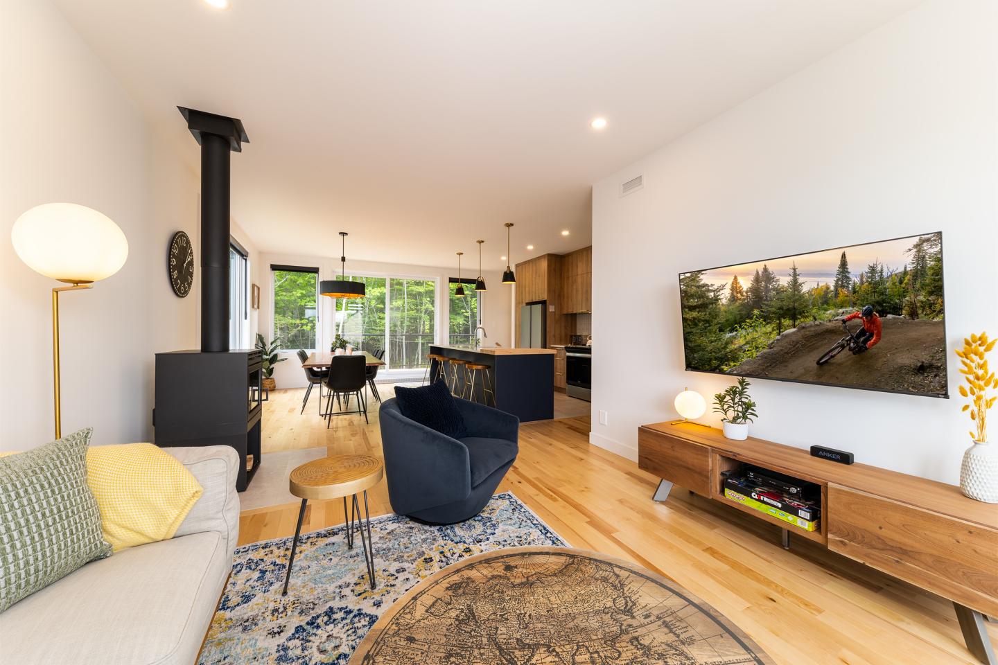 Salon moderne avec canapé, télé murale, et cuisine ouverte au fond.