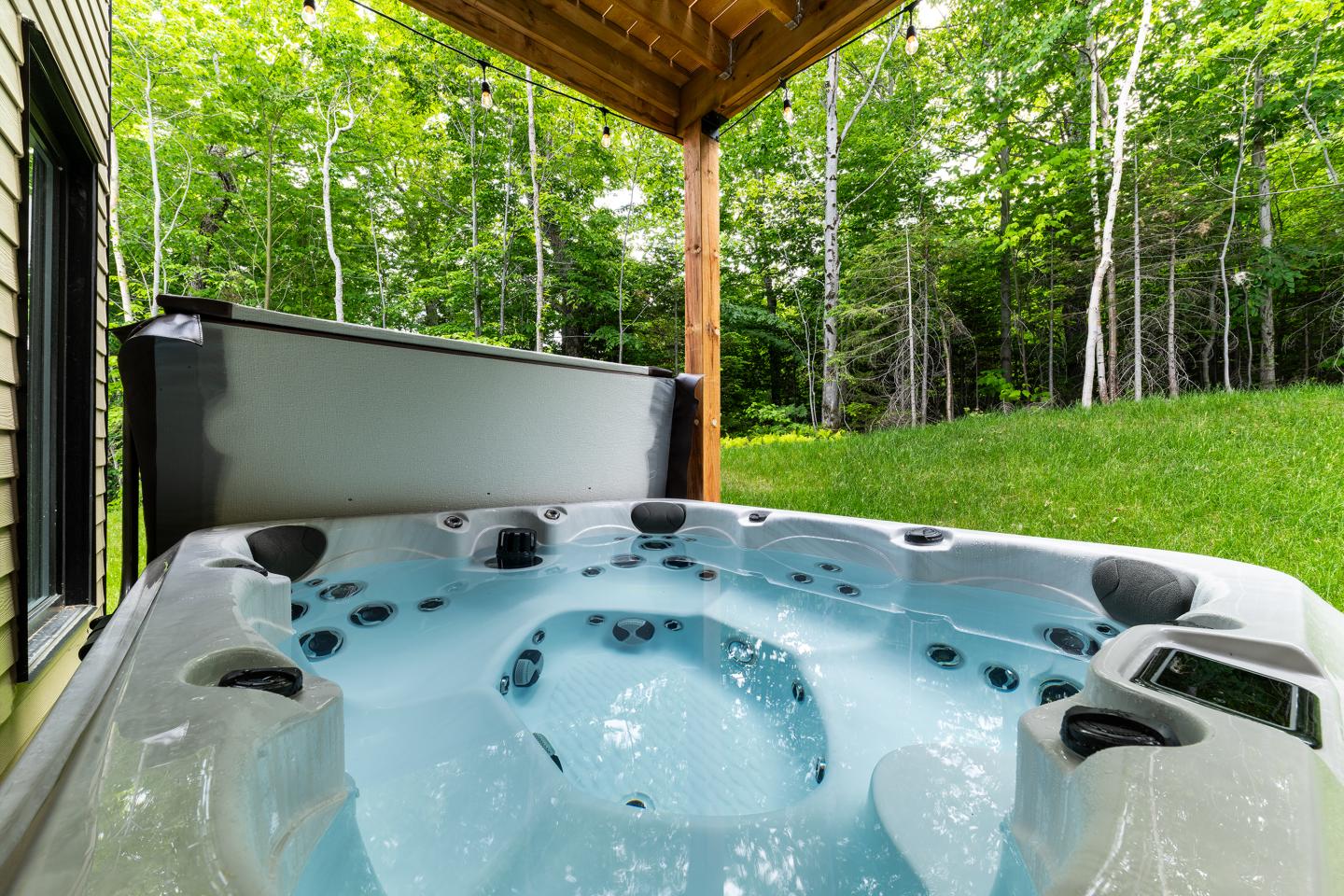 Spa extérieur sous une terrasse en bois, entouré de verdure.