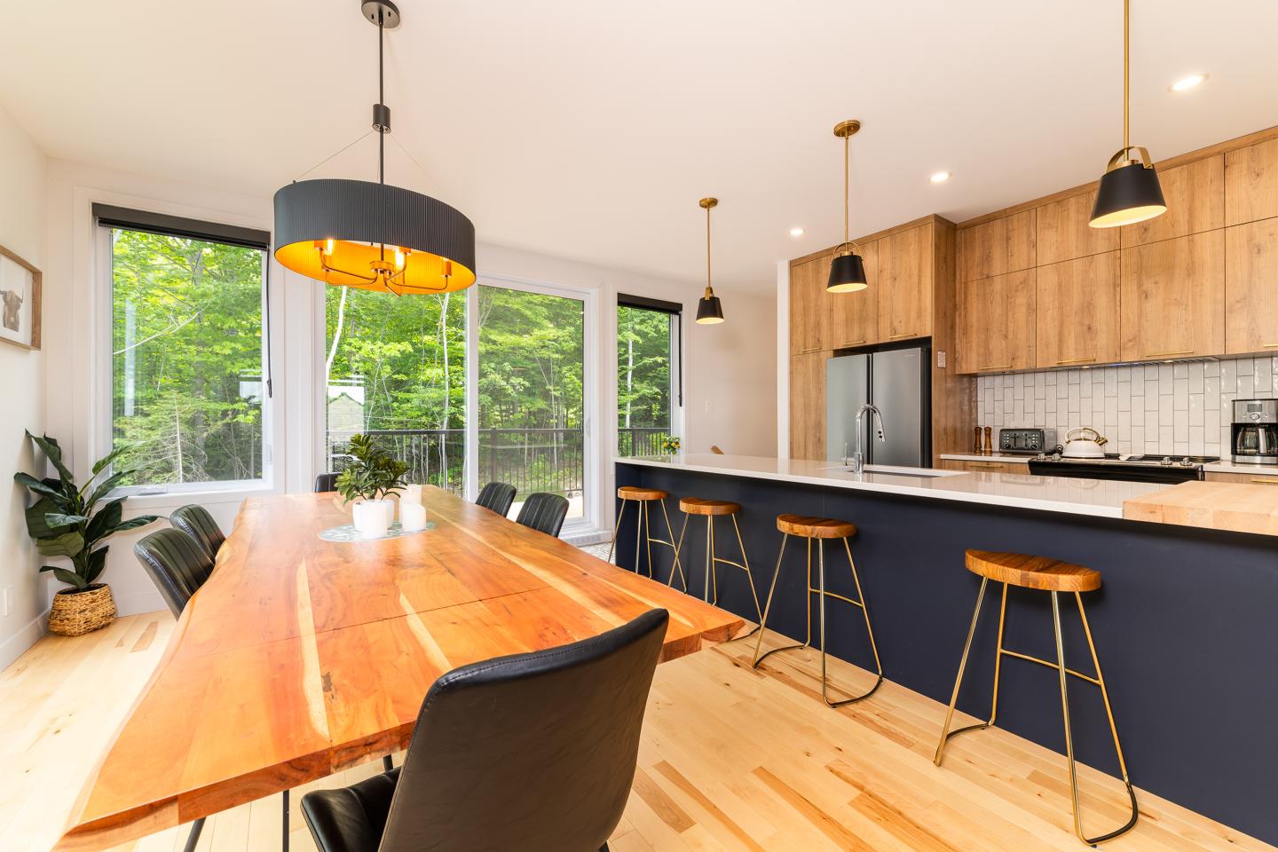 Salle à manger lumineuse, table en bois, chaises noires, cuisine moderne en arrière-plan.