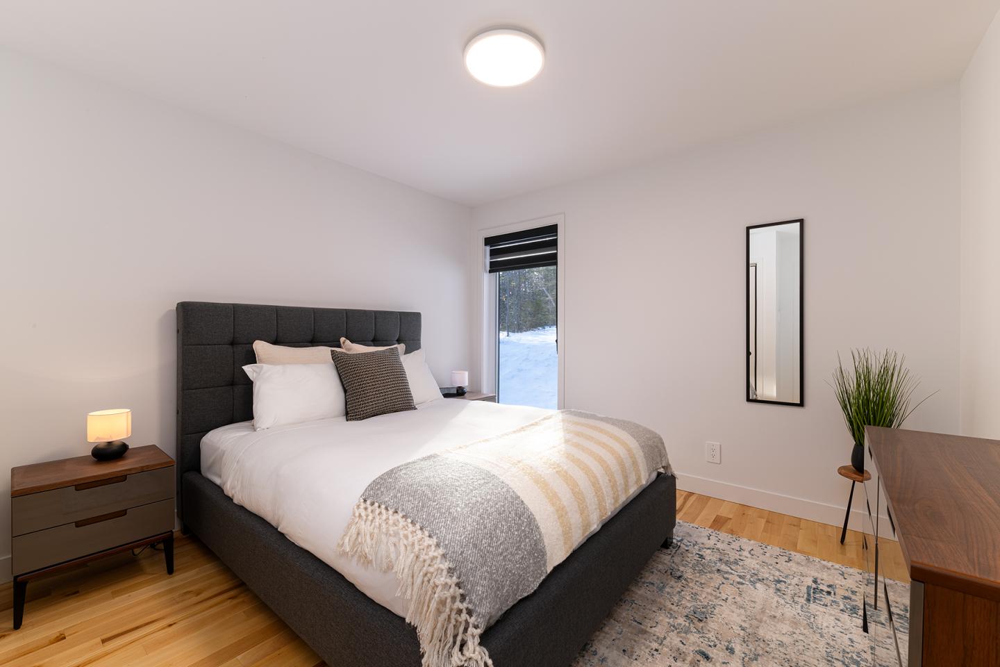 Chambre moderne avec lit double, lampe et miroir sur mur blanc.