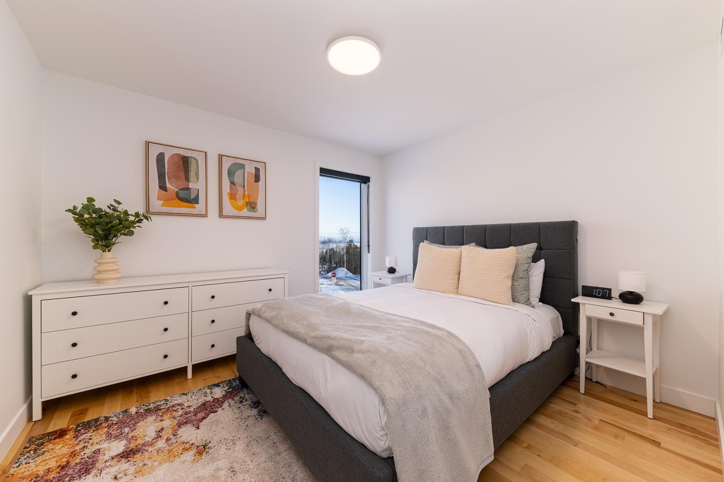 Chambre moderne, lit double gris, commode blanche, déco murale colorée.
