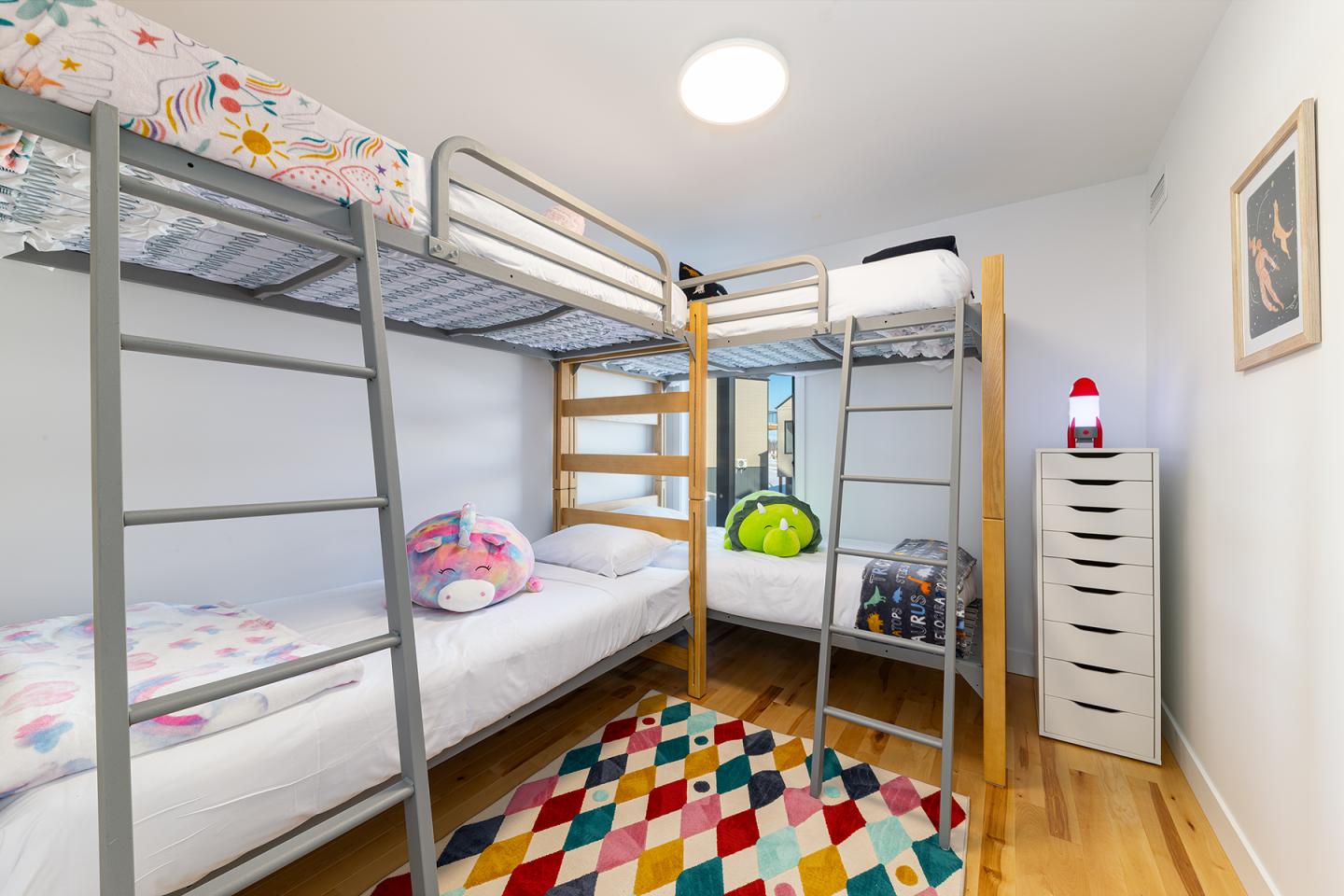 Deux lits superposés, couvre-lits colorés, tiroir blanc, tapis multicolore.
