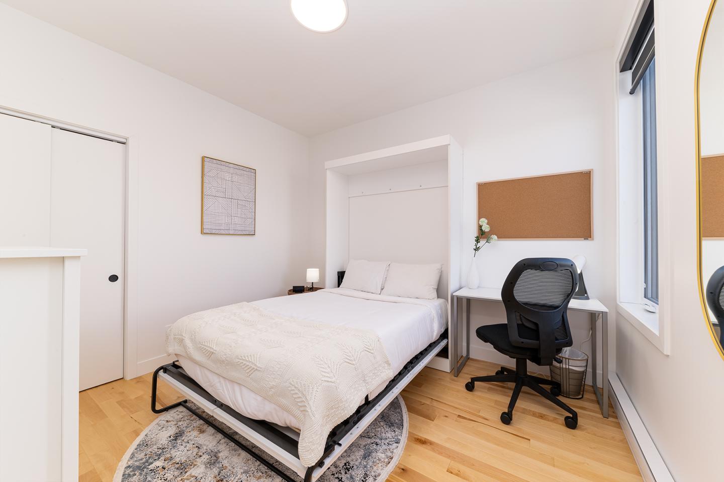 Petite chambre moderne avec lit blanc, bureau et chaise noire.