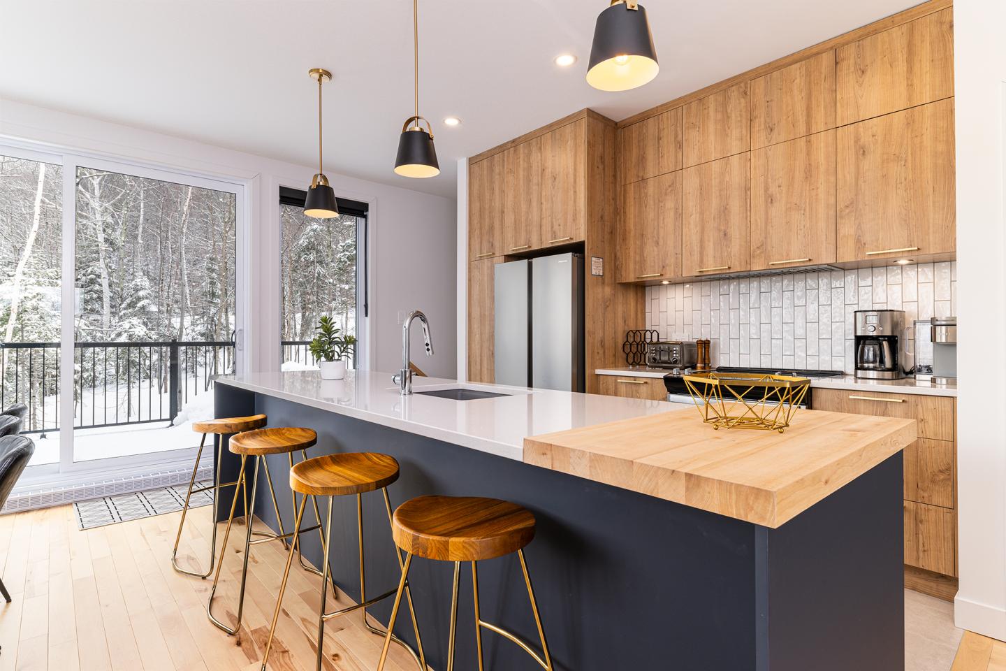 Cuisine moderne avec îlot central et tabourets en bois, vue sur jardin enneigé.