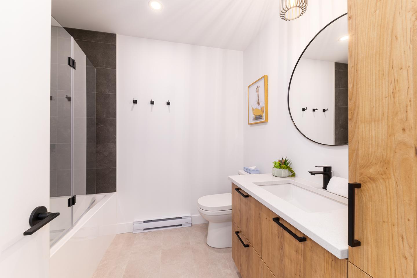 Salle de bain moderne avec lavabo, miroir rond, baignoire et toilette.