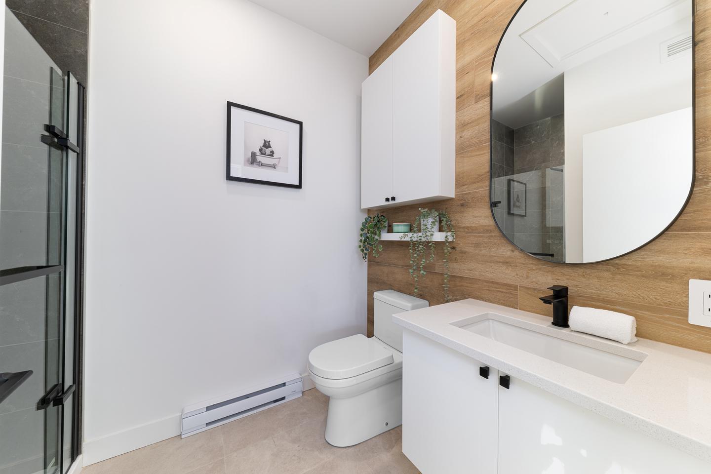 Salle de bain moderne avec lavabo, miroir rond et douche vitrée.