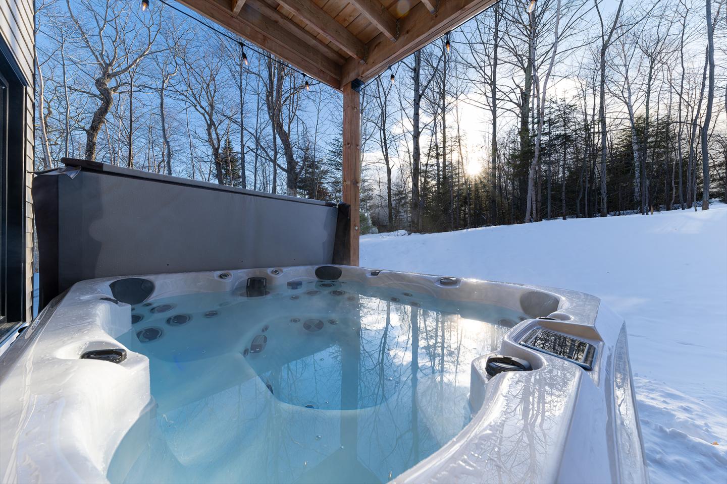 Jacuzzi extérieur entouré de neige sous un ciel bleu ensoleillé.