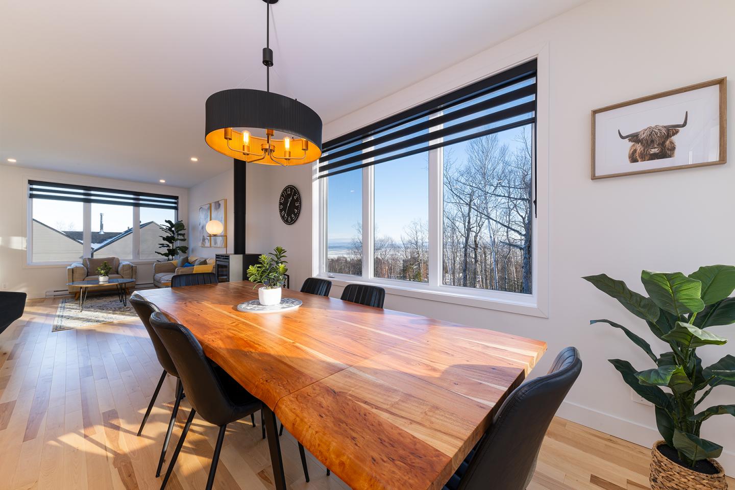 Salle à manger lumineuse avec table en bois, chaises noires, et grande fenêtre.