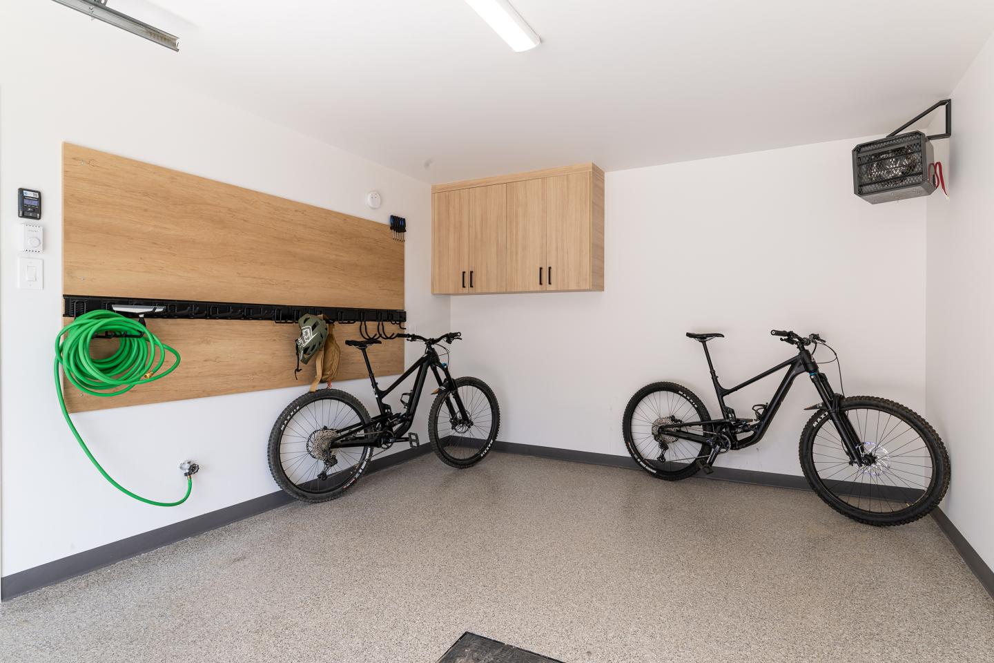 Garage avec deux vélos noirs accrochés au mur, tuyau vert enroulé.