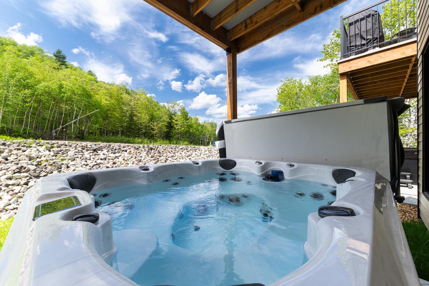 Un jacuzzi sous un patio, entouré de nature verdoyante.
