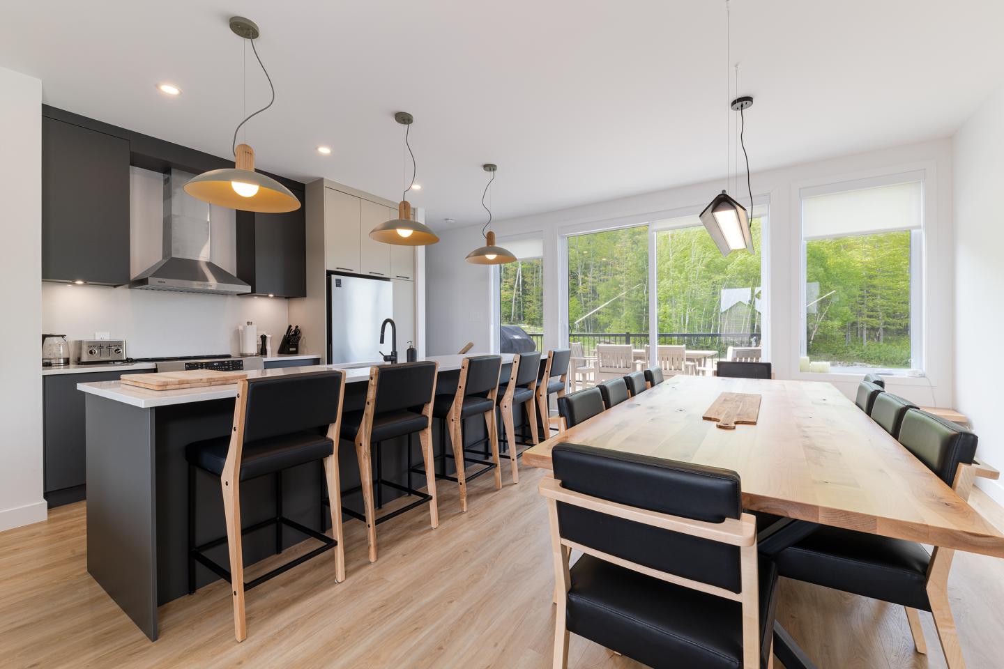 Cuisine moderne avec îlot central, grandes fenêtres et table en bois clair.