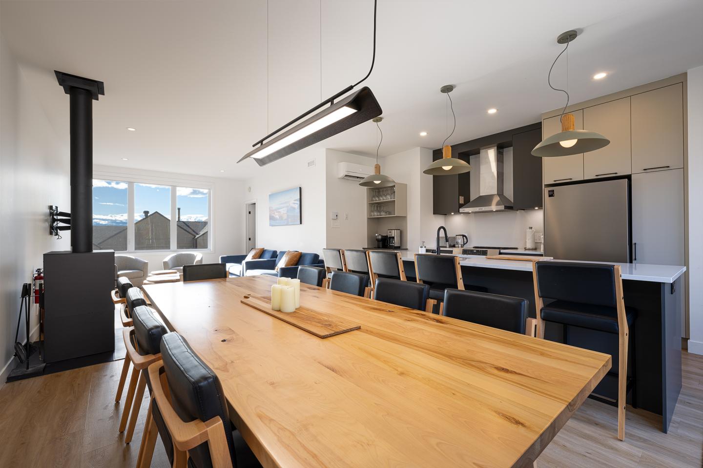 Salle à manger moderne avec table en bois, cuisine ouverte et grandes fenêtres.