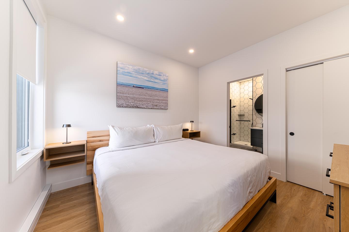 Chambre lumineuse avec lit double, deux lampes, et tableau mural.