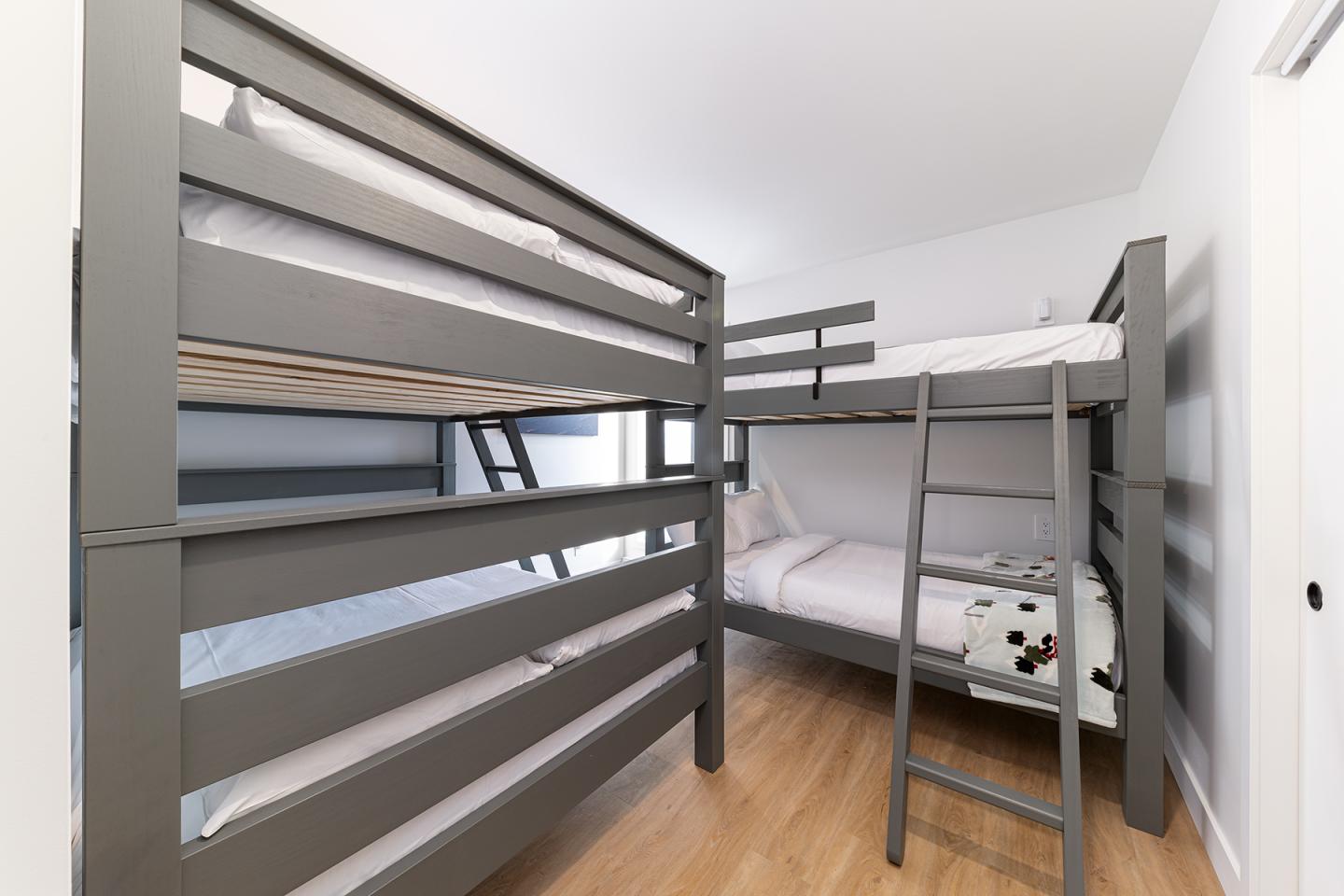 Lits superposés gris dans une chambre lumineuse au sol en bois.