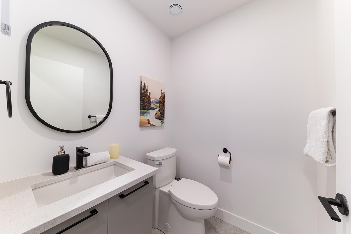 Salle de bains moderne avec miroir ovale, lavabo et toilettes blanches.