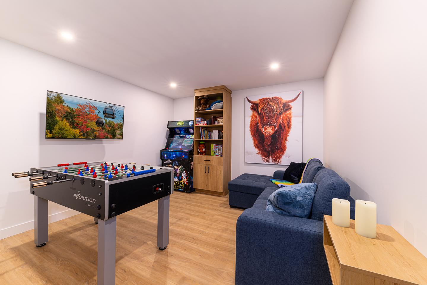 Salle de jeux avec baby-foot, canapé, télévision et étagère.