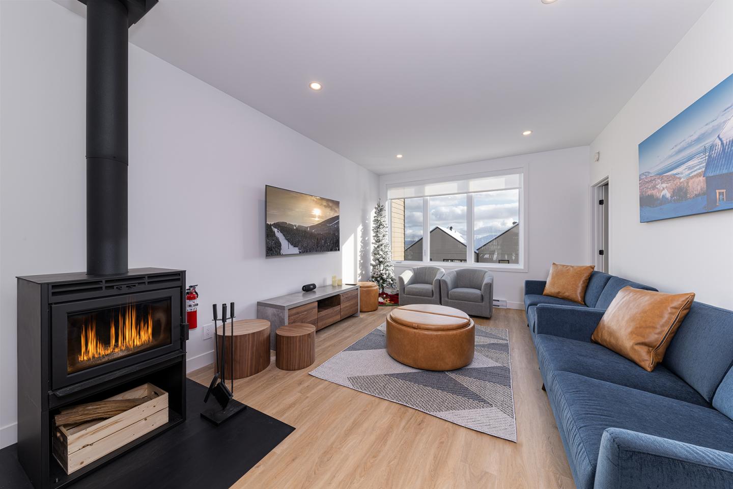 Salon moderne avec cheminée, canapé bleu, et grande fenêtre.