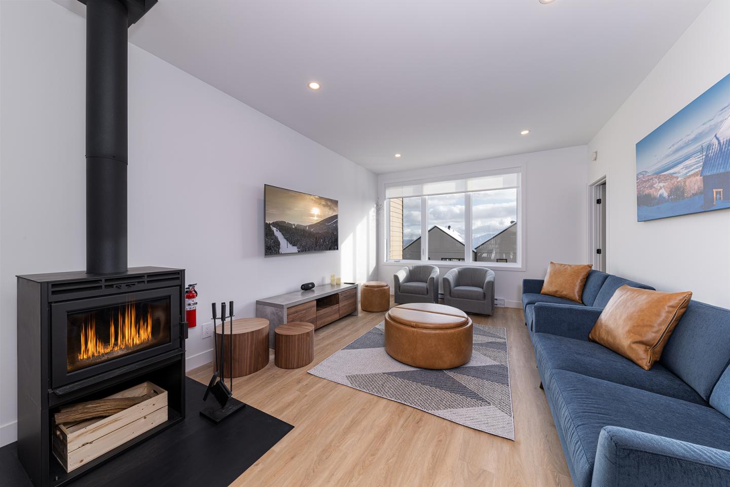 Salon moderne avec cheminée, canapé bleu, et grandes fenêtres.
