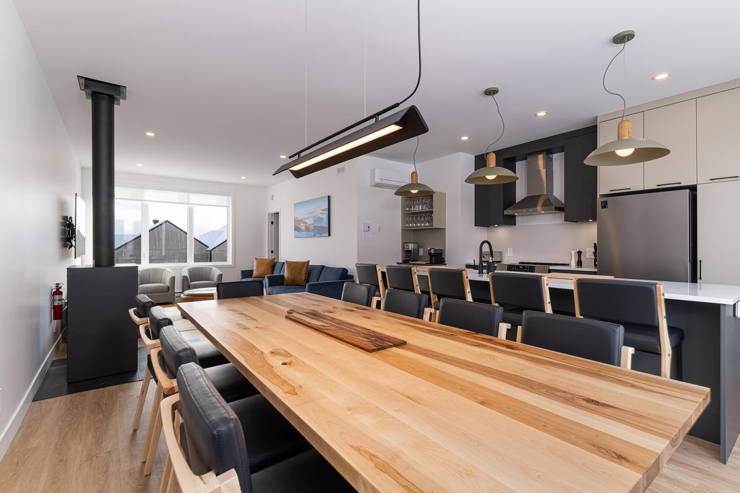 Salle à manger moderne avec table en bois, chaises noires et cuisine ouverte.