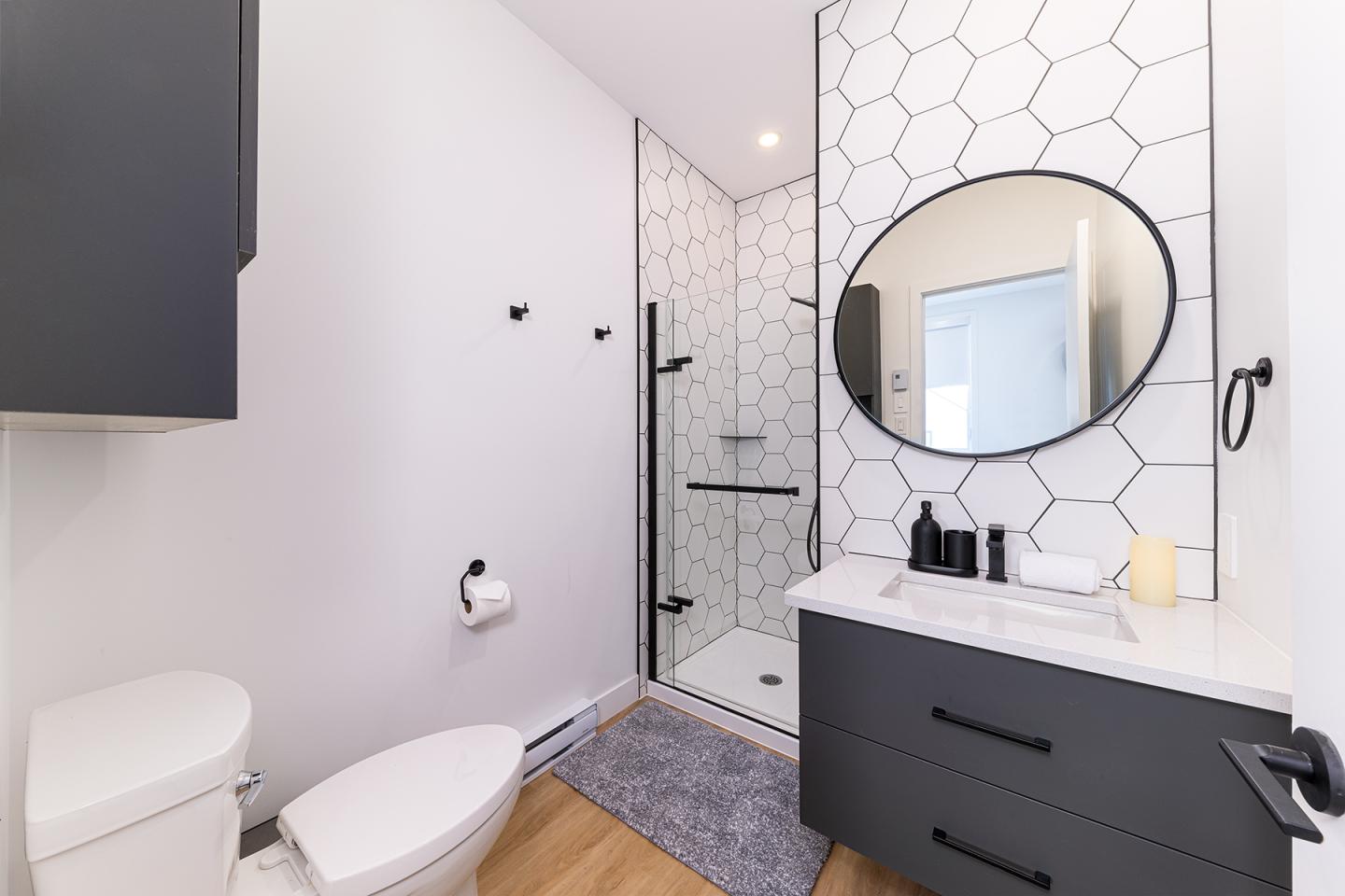Salle de bain moderne avec douche vitrée, lavabo noir, miroir rond.