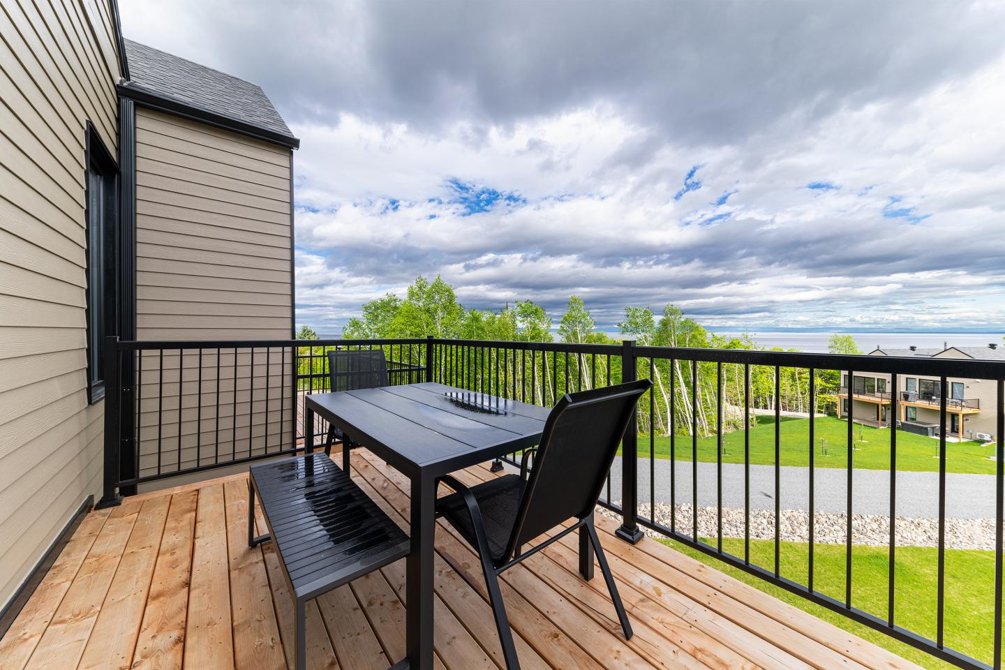 Table et chaises sur balcon en bois avec vue sur jardin, ciel nuageux.
