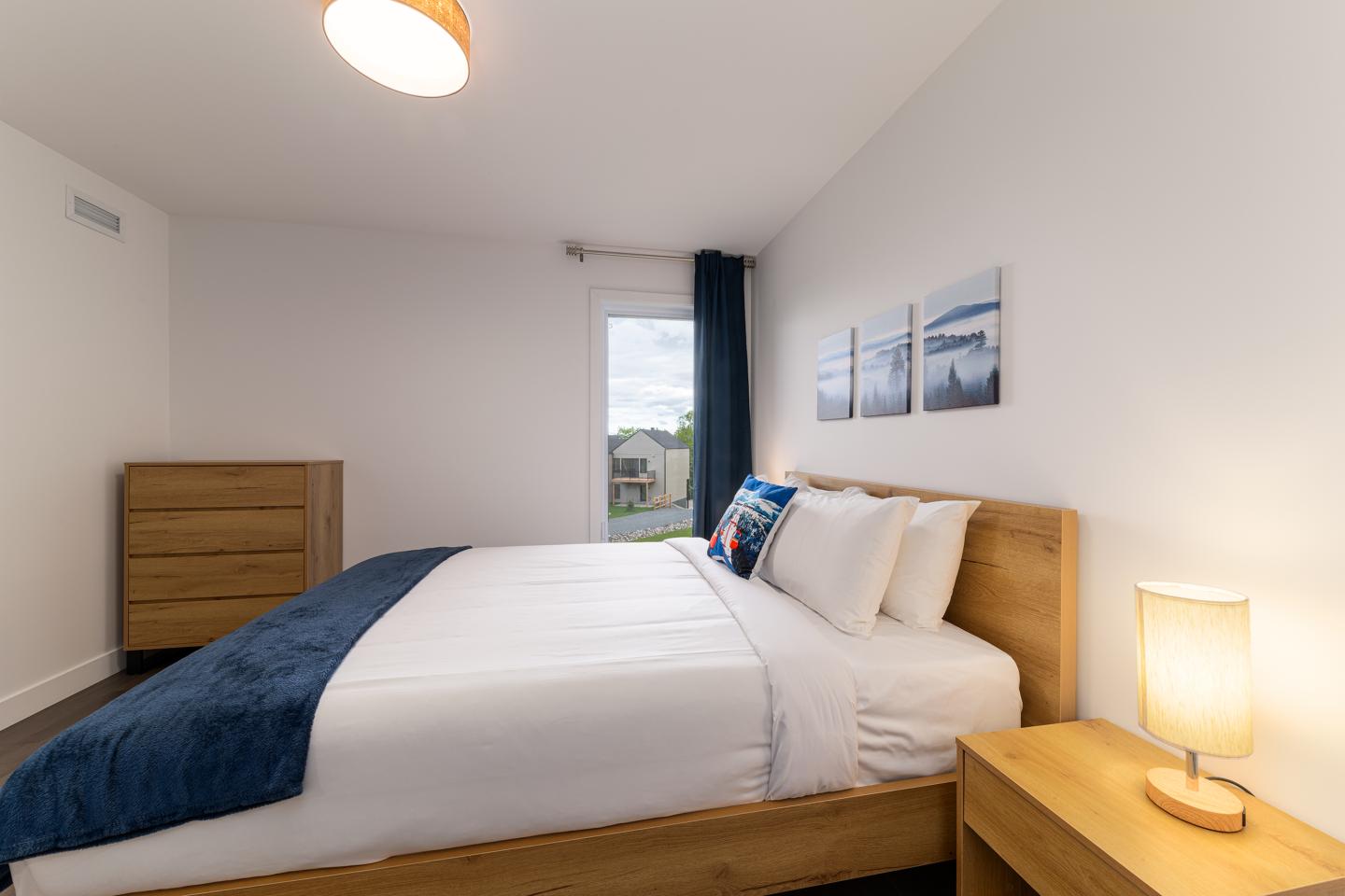 Chambre moderne, lit double avec couverture bleue, lampe et tableaux.