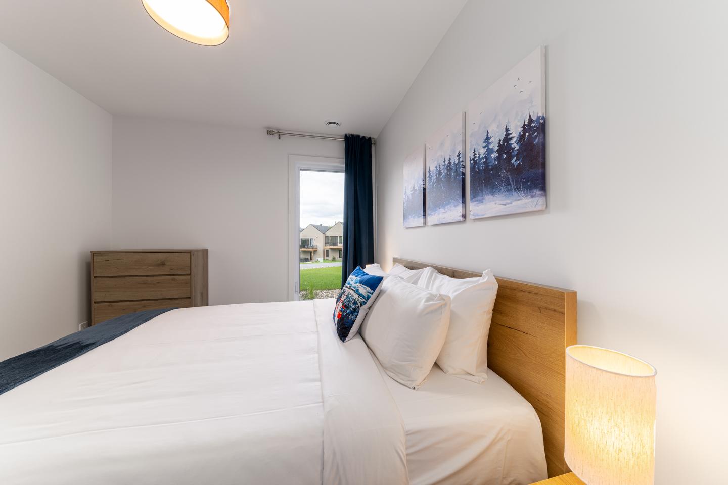 Chambre moderne, lit blanc, tableaux muraux, fenêtre avec rideaux.