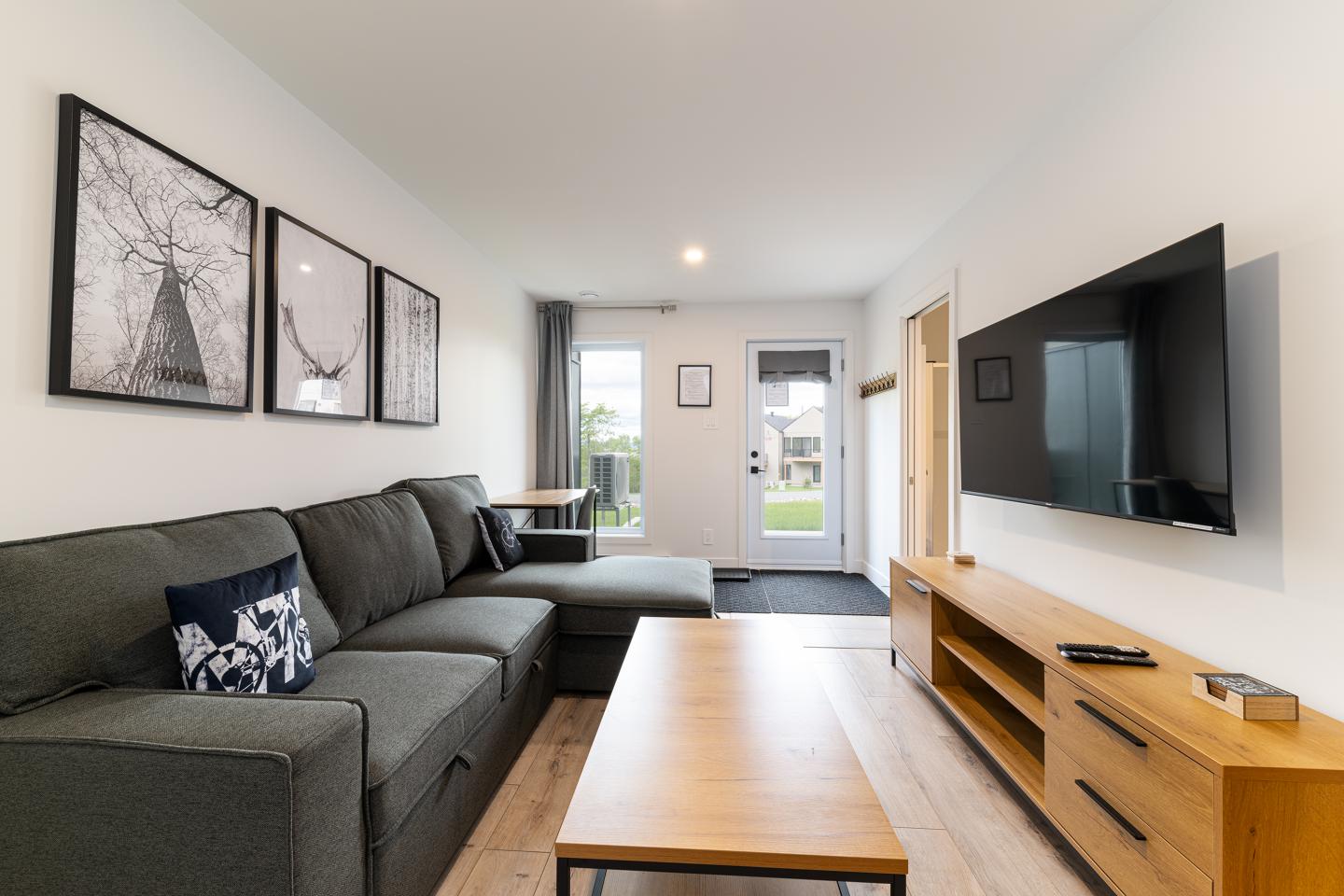 Salon moderne avec canapé gris, TV murale et table basse en bois.