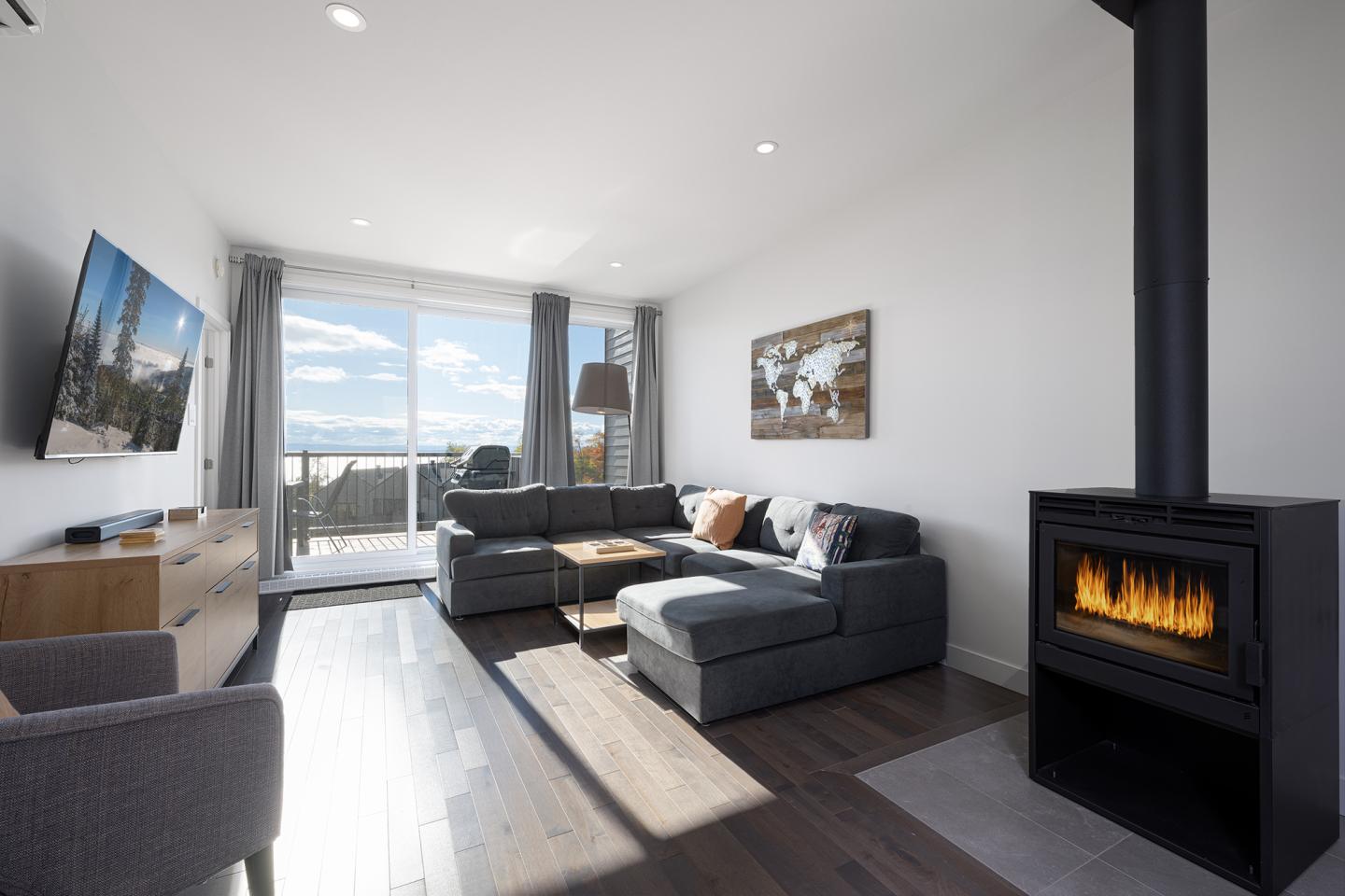 Salon moderne avec cheminée, canapé gris, télé écran plat et grande fenêtre.