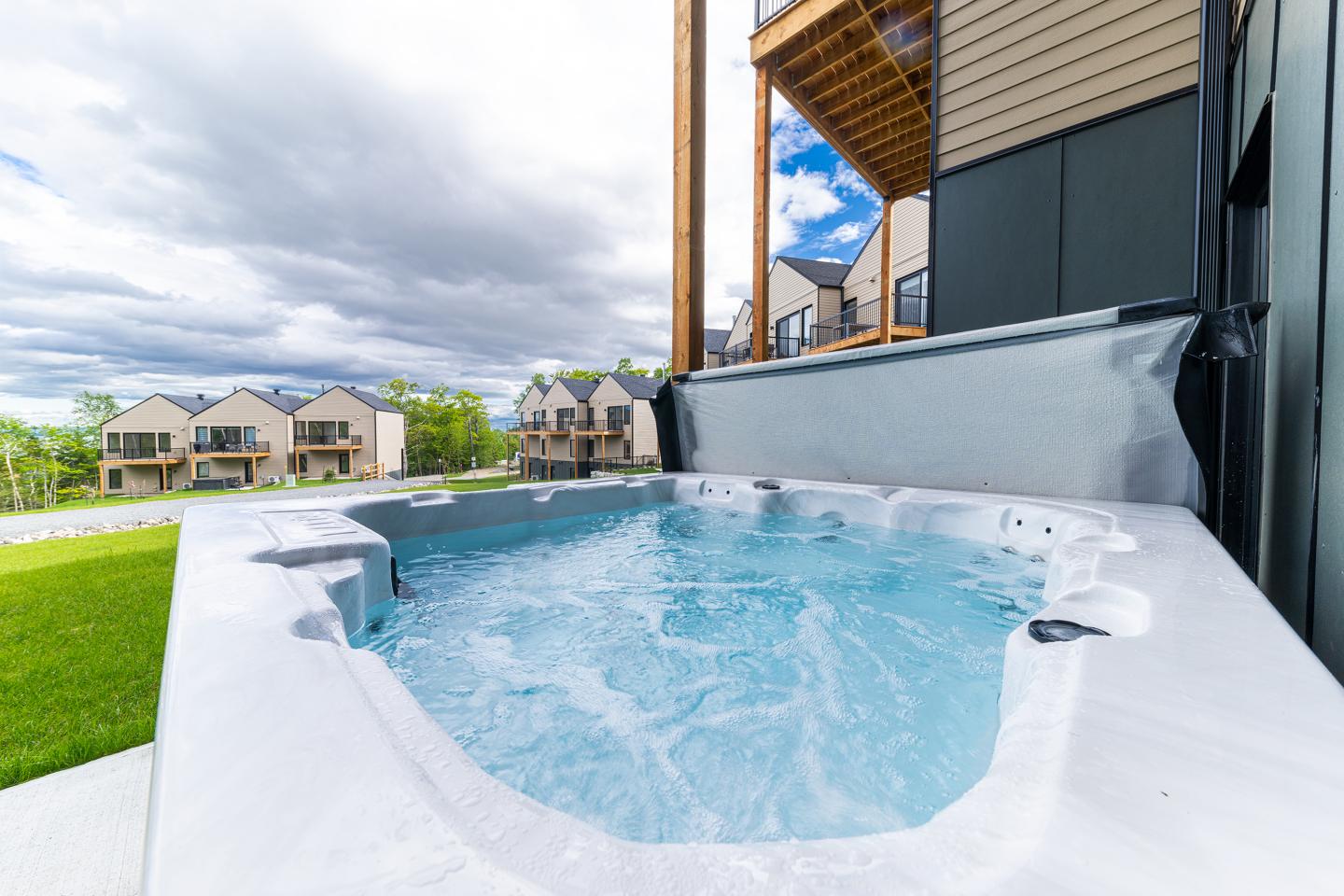 Spa bouillonnant extérieur avec maisons en arrière-plan sous un ciel nuageux.