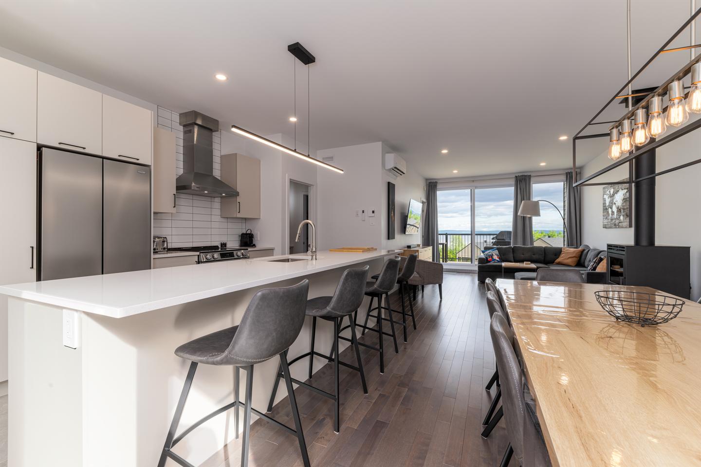 Cuisine moderne avec îlot, table en bois, et vue sur le salon et la terrasse.