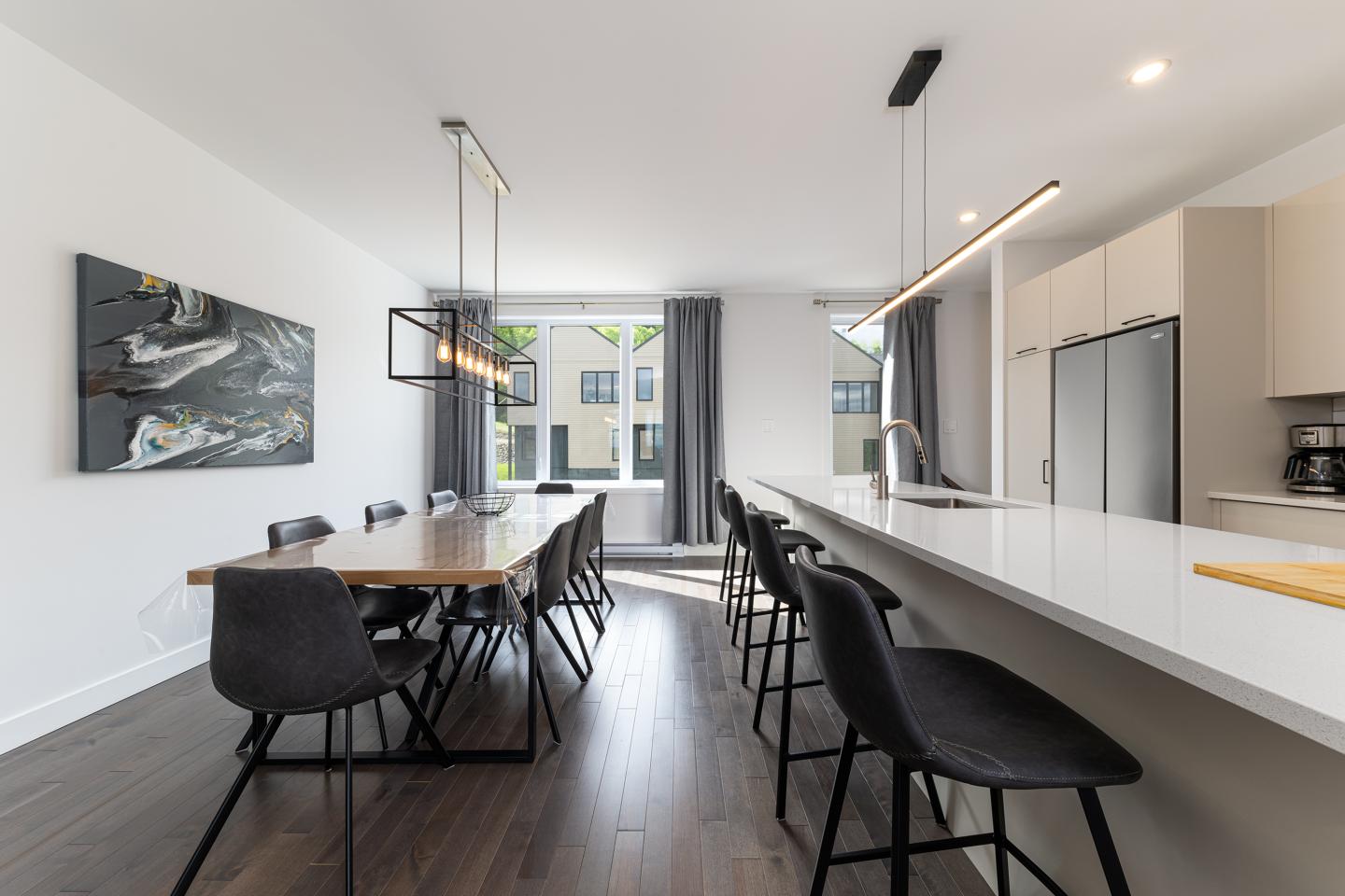 Salle à manger moderne avec table en bois, chaises noires, et cuisine blanche.