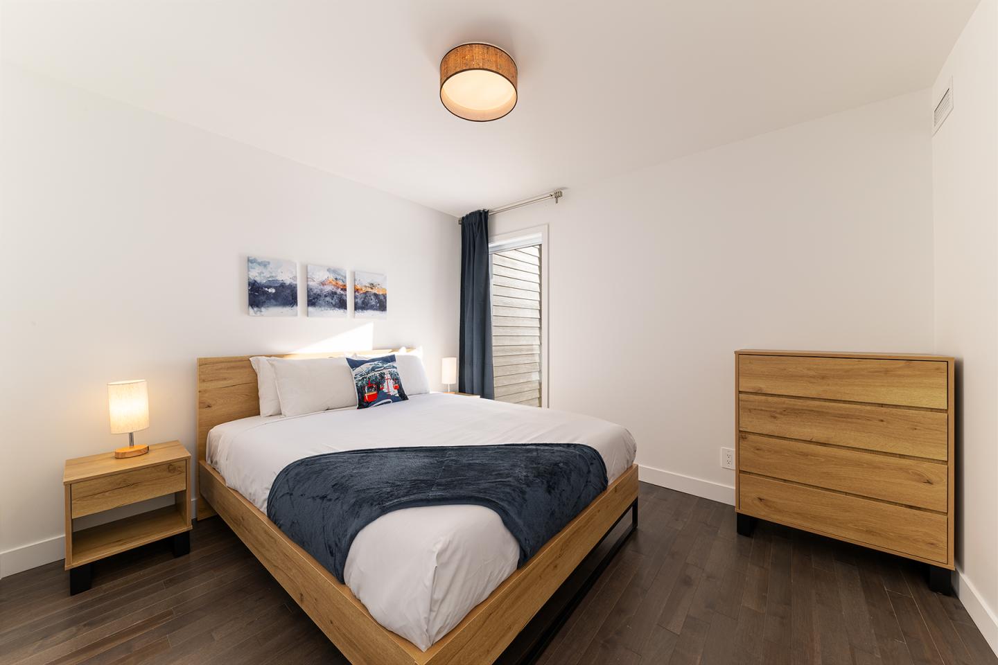 Chambre moderne avec lit double, deux lampes et commode en bois.