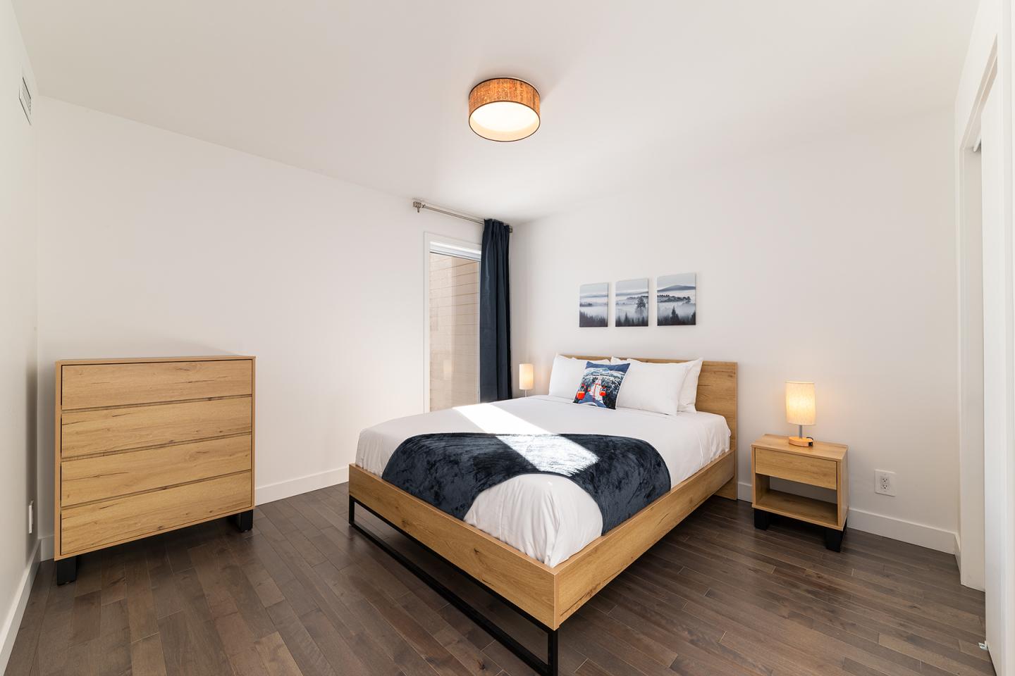 Chambre moderne avec lit double, commode en bois et lampes allumées.
