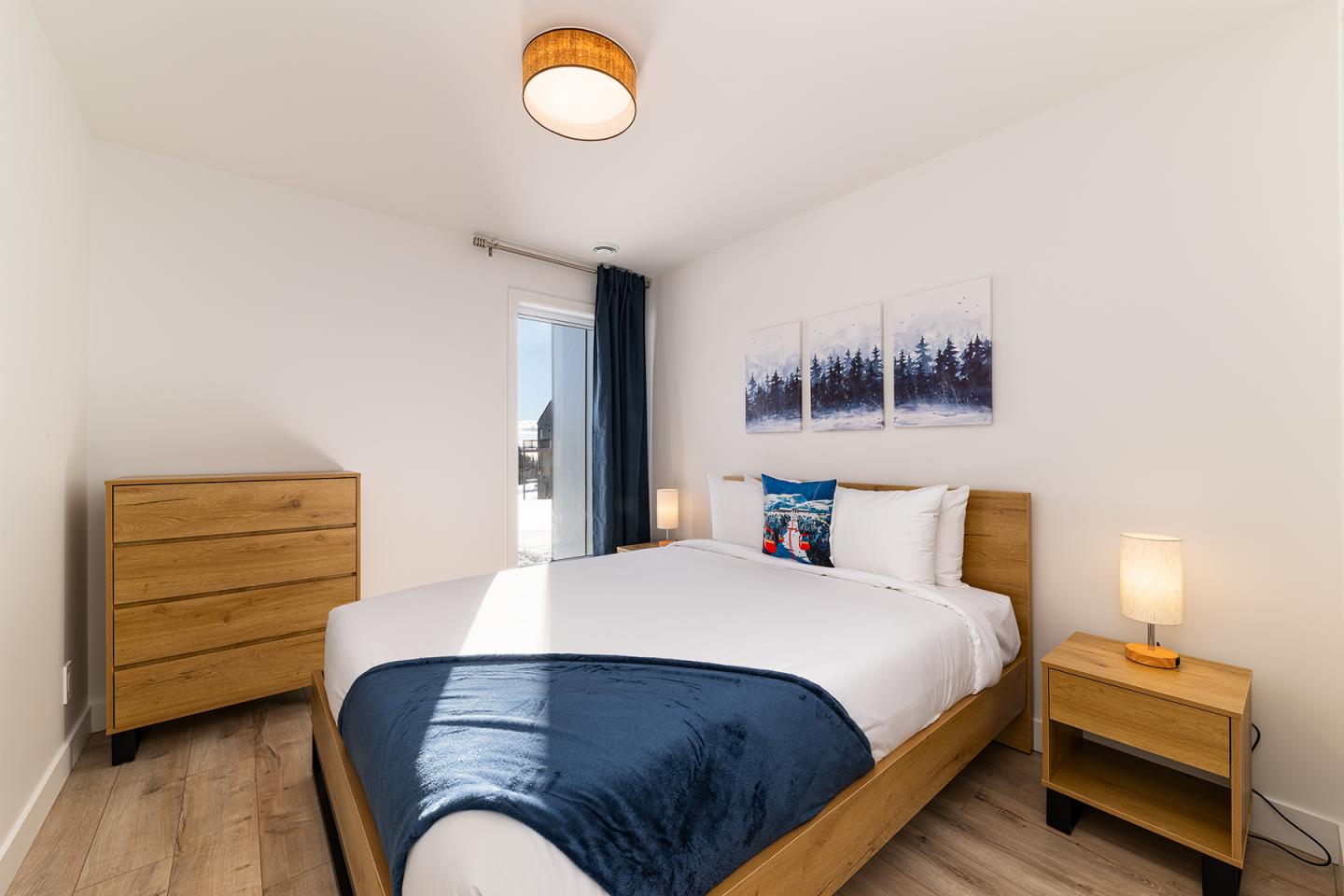 Chambre moderne avec lit double, couvre-lit bleu, et meubles en bois clair.