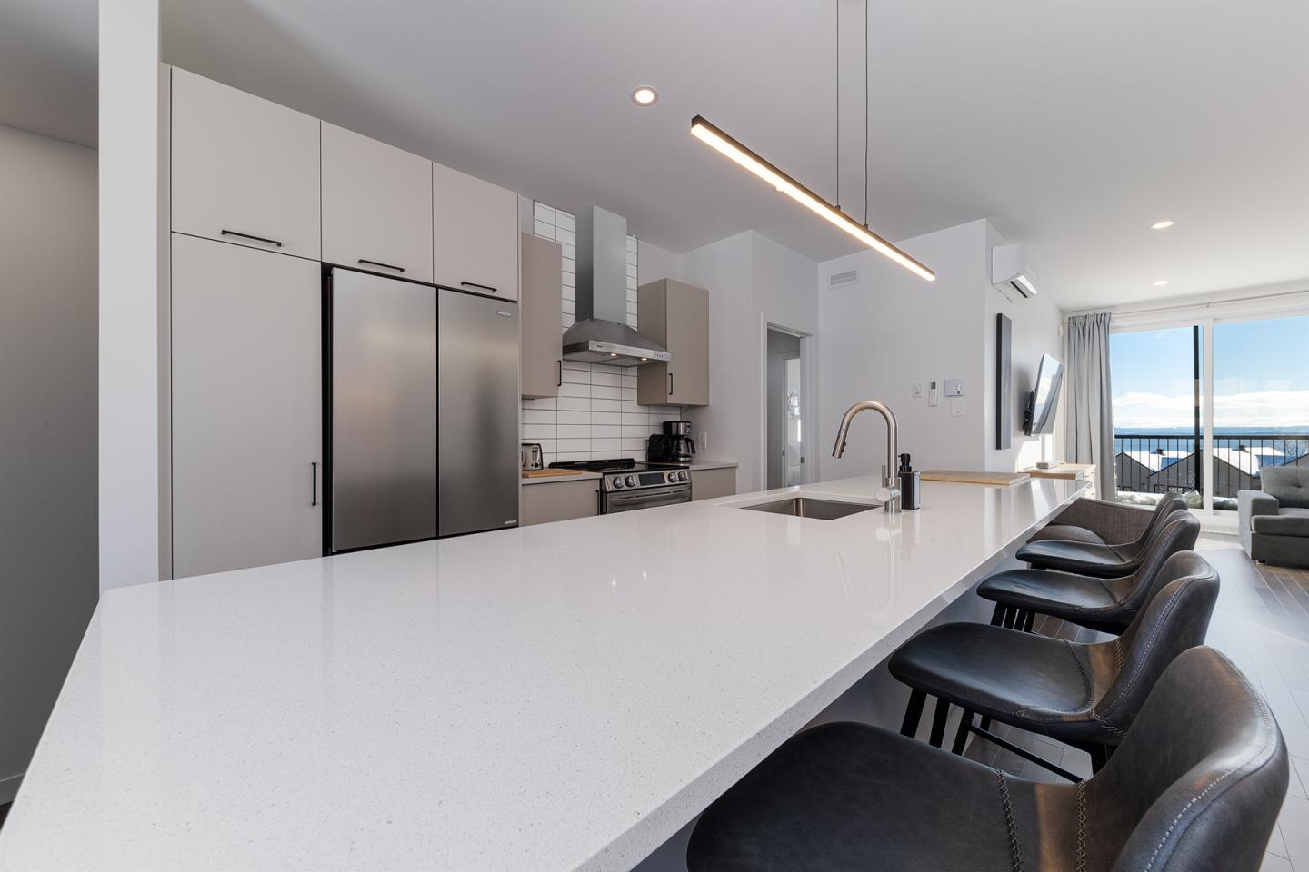 Cuisine moderne avec îlot blanc, chaises noires et éclairage élégant.