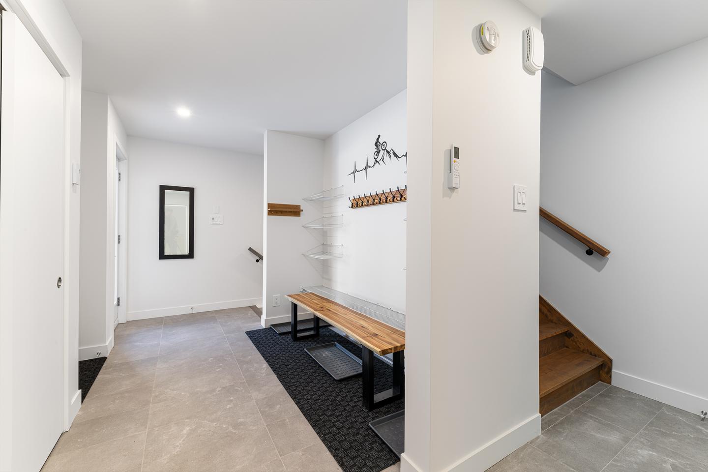 Couloir moderne avec banc en bois, crochets muraux, et escalier à droite.