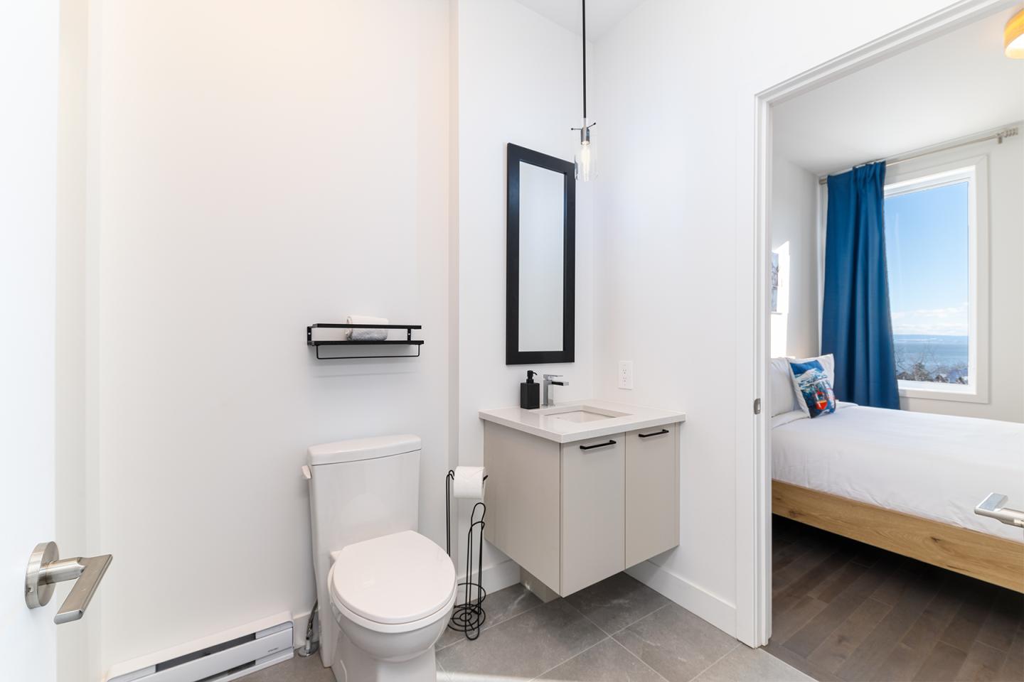 Salle de bain moderne avec toilettes, lavabo et vue sur chambre lumineuse.