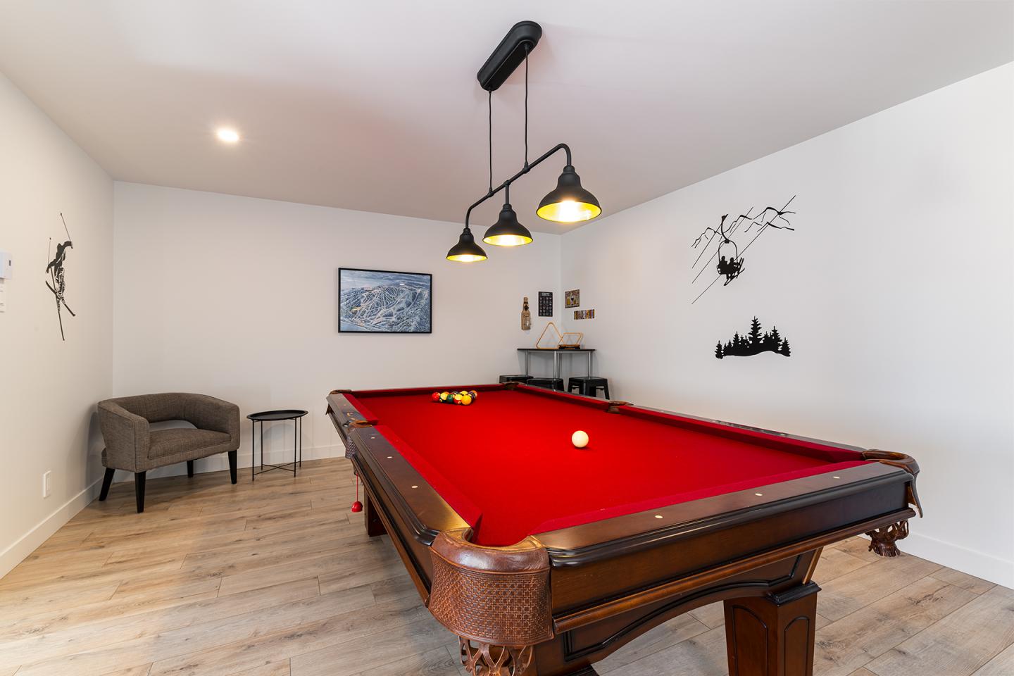 Salle avec table de billard rouge, chaises, et décor mural. Éclairage suspendu au plafond.