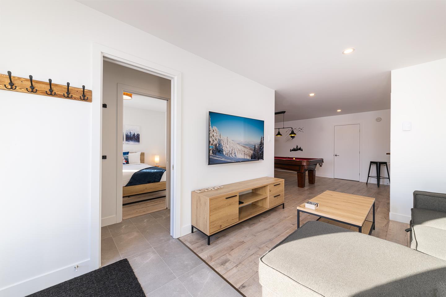 Salon moderne avec canapé, table basse, télévision et porte ouverte vers une chambre.