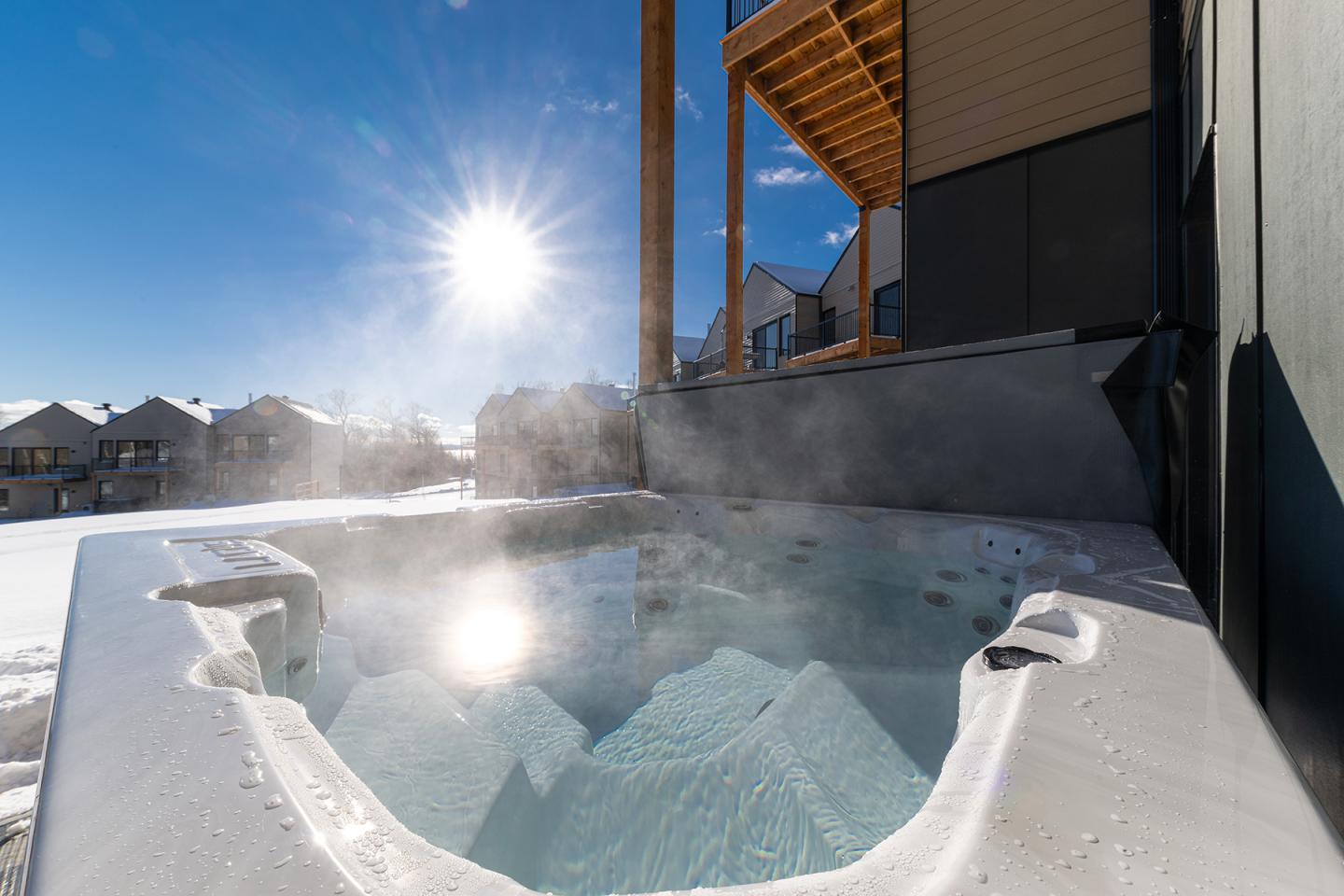 Jacuzzi extérieur sous le soleil d'hiver, avec maisons en arrière-plan.
