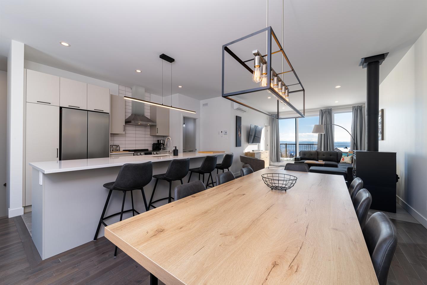 Cuisine moderne avec îlot, table en bois, et salon au fond.