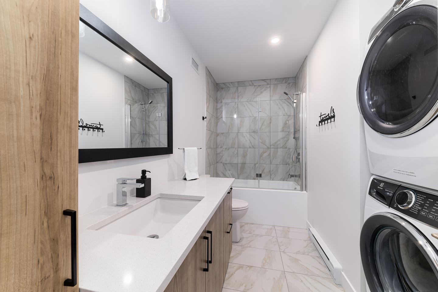 Salle de bain moderne avec lave-linge, sèche-linge, et baignoire.