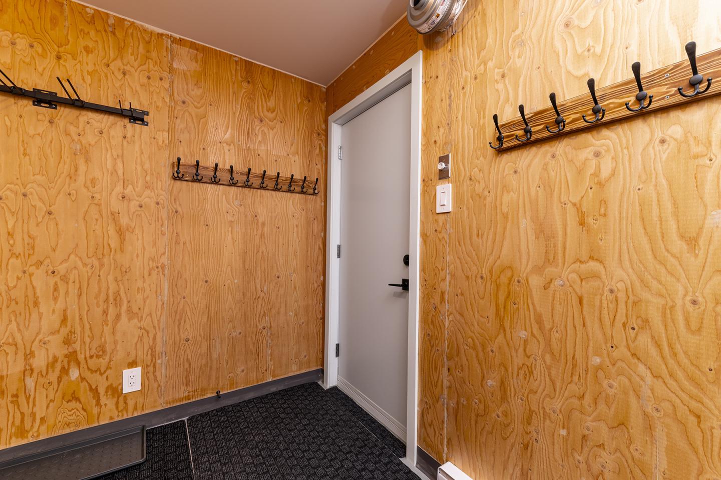 Vestiaire en bois avec crochets et porte grise.