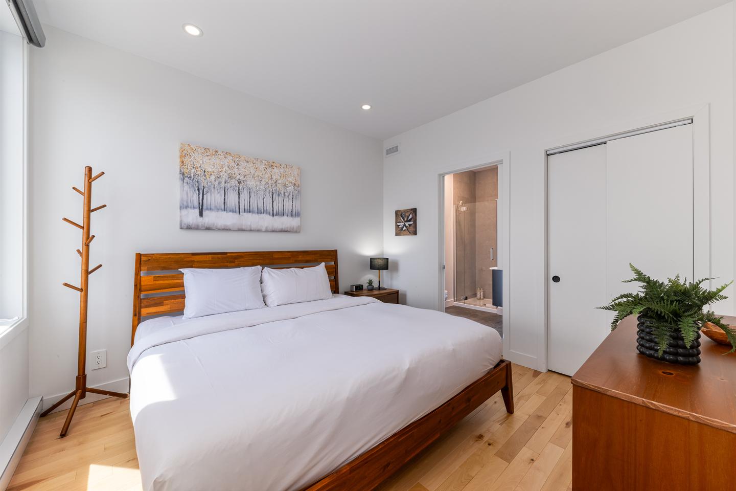 Chambre moderne avec lit double, tableau, plante et parquet clair.
