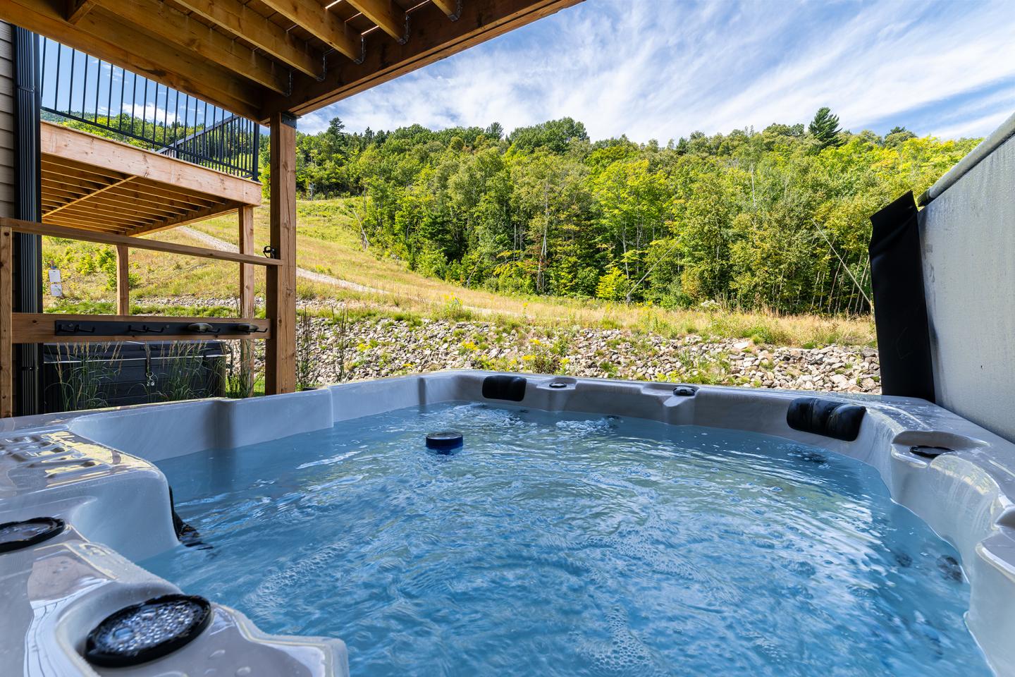 Spa extérieur avec vue sur colline boisée sous ciel bleu.