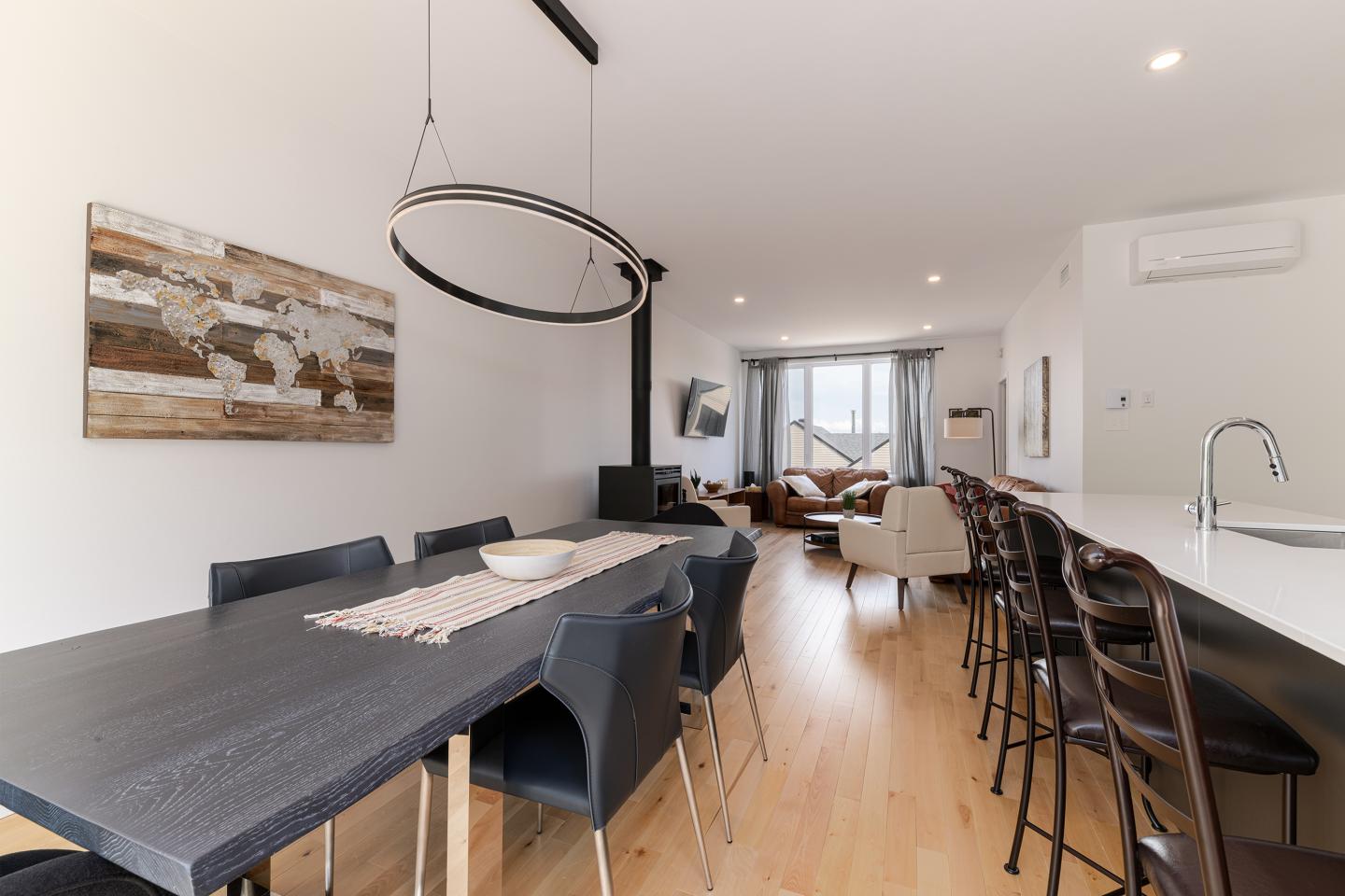 Salle à manger moderne avec table noire et hauts tabourets, mur blanc.