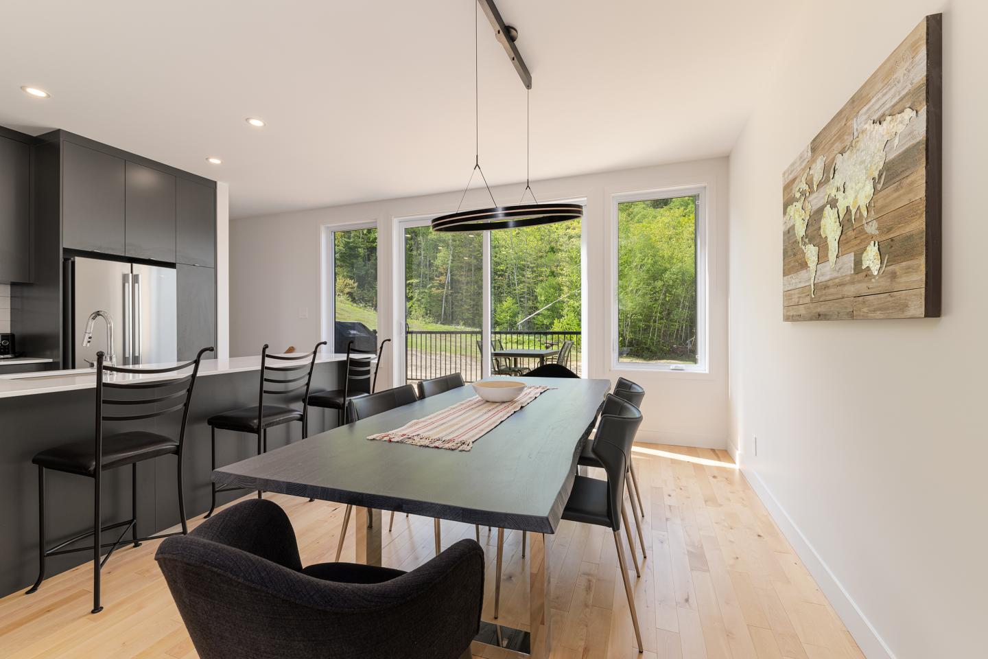 Salle à manger moderne avec table noire, chaises et vue sur jardin verdoyant.