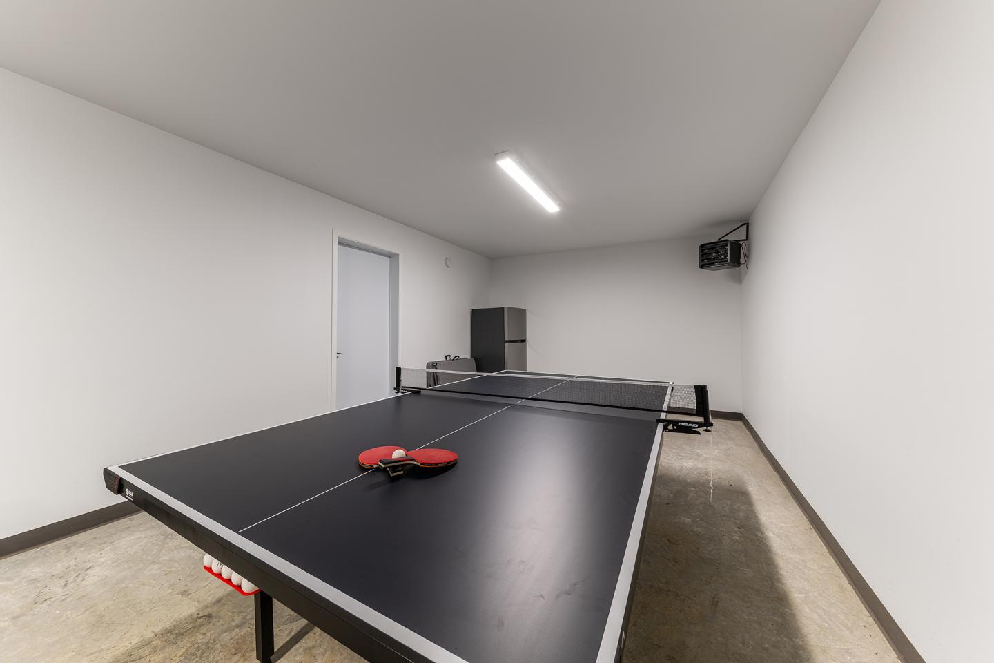 Table de ping-pong noire dans une salle blanche, raquette rouge posée dessus.