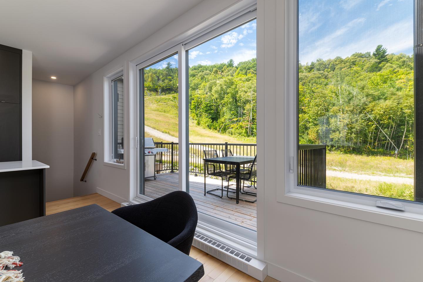 Salle à manger moderne avec vue sur terrasse et colline verdoyante.